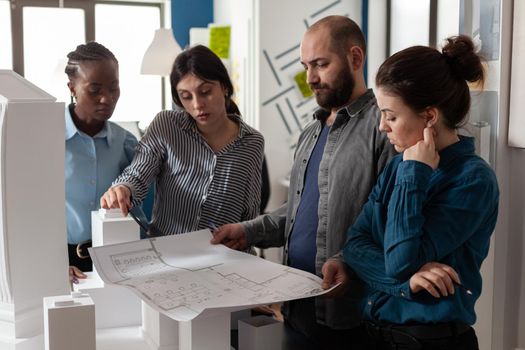 Team of multi ethnic architects designing blueprint plan for construction project design. Workers analyzing maquette buildng model engineering technology at professional office.