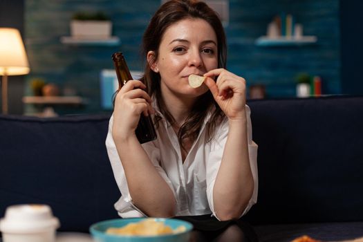 Portrait of woman looking into camera eating tasty delicious snack enjoying takeaway food home delivered. Caucasian female relaxing on sofa late at night in living room. Fastfood lunch meal order