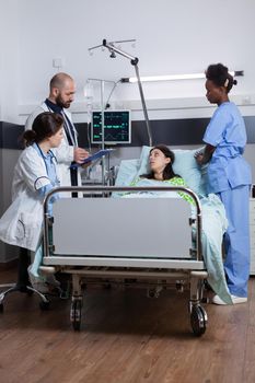 Practitioners doctors checking sick woman writing disease treatment on clipboard during medical appointment in hospital ward. Patient lying in bed with nasal oygen tube discussing sickness symptom