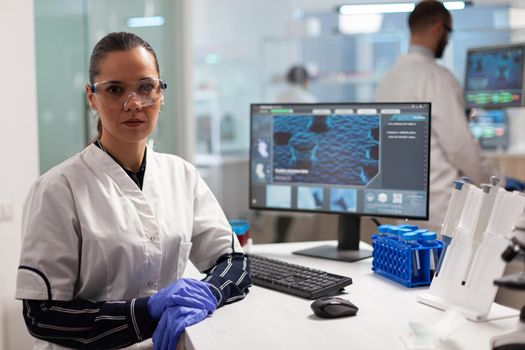 Laboratory doctor looking at camera smiling in modern equipped lab. Examining virus evolution using high tech and chemistry tools for scientific research, vaccine development.