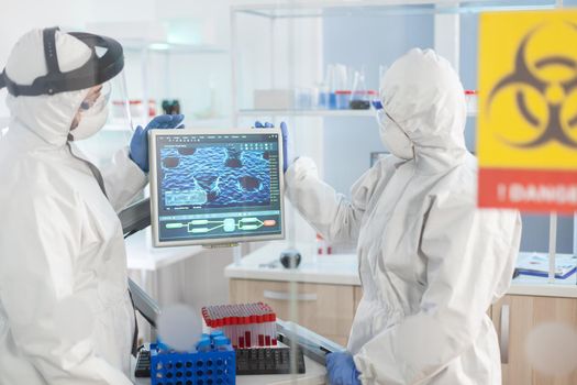 Team of scientist looking at virus evolution standing in lab danger zone dressed in ppe suit. Group of doctors examining vaccine evolution using high tech for diagnosis against covid19.