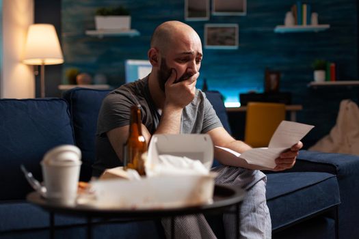 Desperate frustrated stressed young man reading letter, payment debt notification, bad financial report, eviction renter notice. Anxious, worried tenant by warning document for unpaid bank bills