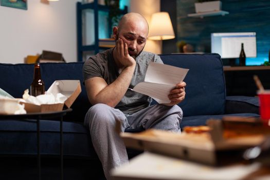 Desperate frustrated stressed young man reading letter, payment debt notification, bad financial report, eviction renter notice. Anxious, worried tenant by warning document for unpaid bank bills