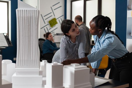 Professional architecture multi ethnic women working on blueprints and building model maquette construction design. Team of workers pointing at architectural paper plan as occupation