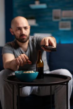 Scared shocked man looking at horror thriller movie at tv, eating popcorn trembled with fright sitting on comfortable sofa. Concentrated alone male watching tv late night enjoying free time