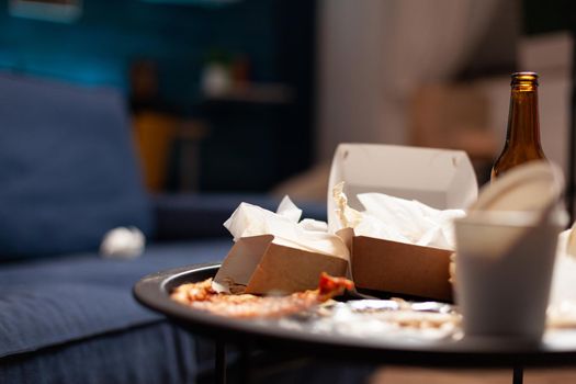 Dirty empty living room with food trash, bottle of beer and napkins on blue sofa. Unorganized house apartment of lonley woman with anxiety depresion having garbage, rubbish with no people in