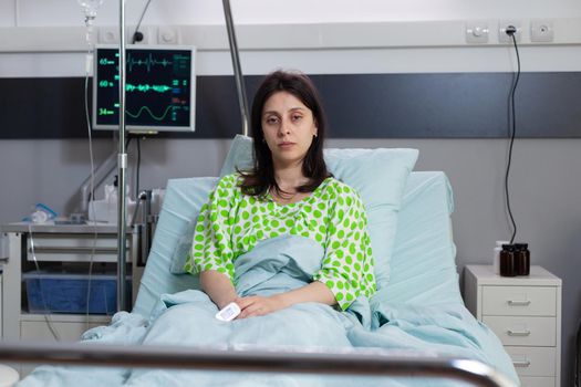 Sick woman looking into camera lying in bed recovering after respiratory surgery. Patient with breathing disorder waiting for sickness treatment in hospital ward