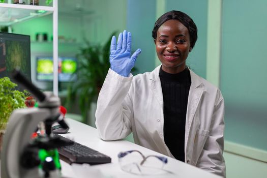 Pov of african woman sitting at desk table in pharmaceutical laboratory during online videocall meeting. Specialists team researching genetic mutation developing dna GMO biology test.