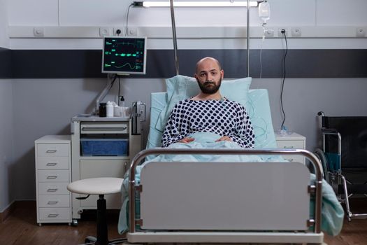 Potrait of depressed sick man lying in bed waiting for respiratory treatment recovering after medical surgery in hospital ward. Hospitalized patient looking into camera wearing nasal oxygen tube