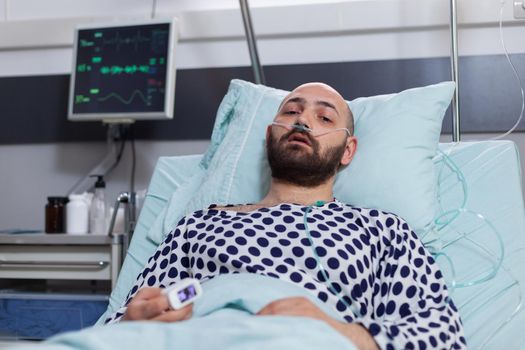 Potrait of sick man wearing nasal oxygen tube having respiratory disease lying in bed during recovering treatment. Patient waiting for physician while looking at camera in hospital ward