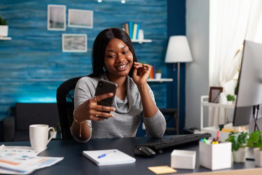 Student with dark skin discussing communication course with remote collegue during online videocall meeting conference using phone. African american woman working remote from home