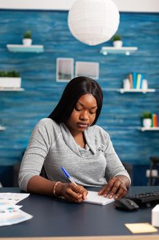 African american student working remote from home studying math lesson writing academic homework on notebook. Black student sitting at desk in living room during university education webinar