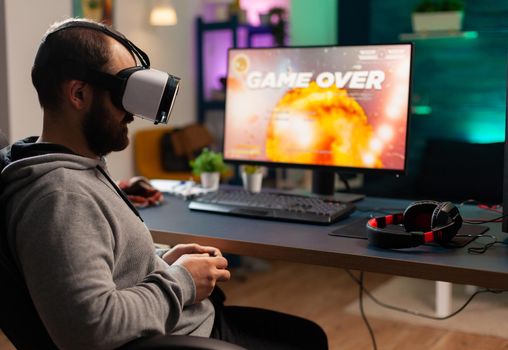 Concentrated gamer wearing virtual reality headset losing space shooter games on online. Defeated player using controller for online competition late at night in gaming room