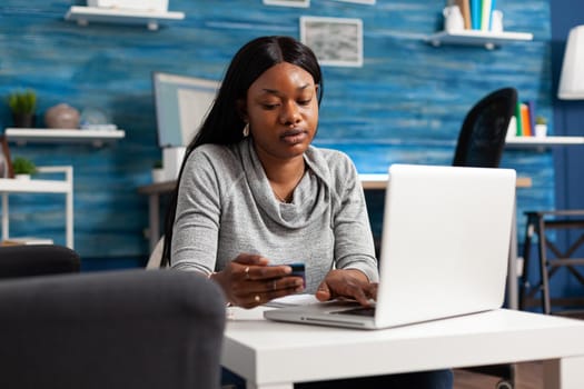 Afro american student sitting on bean bag in living room holding credit card paying sale shopping order making online digital transaction. Black woman using internet banking service at home