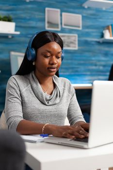 African american student wearing headset browsing online information working at communication webinar in living room. Black woman blogger composing social media article putting on blog
