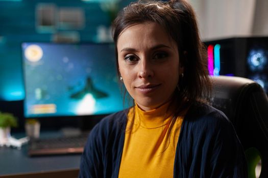 Portrait of woman gamer looking into camera after playing space shooter games using professional RGB keypad on powerful computer. Caucasian pro player streaming online videogames in home studio