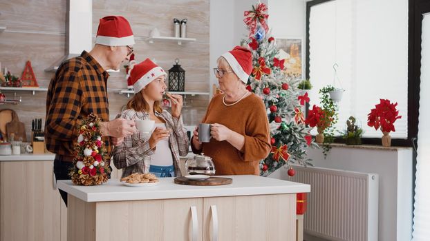 Happy family wearing santa hat celebrating christmas day holiday eating baked chocolate cookies in xmas decorated kitchen. Grandparents enjoying spending time with granddaughter during winter season