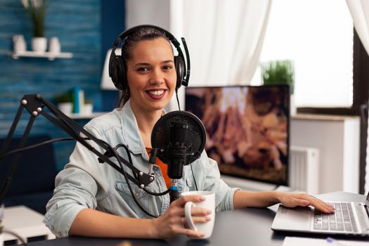 Smiling influencer woman sitting in front of camera recording video for fashion blog. Digital blogger vlogger streaming talk show in studio using headphones, professional podcast microphone