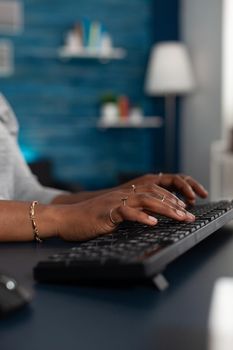 Close-up of black student hands typing on keyboard browsing online information on internet working remote at business article sitting at desk table. African american woman searching education email