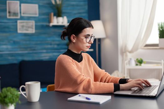 Student college browsing marketing advertising for school homework typing information on keyboard using laptop computer. Woman looking at e-learning university platform while sitting at desk