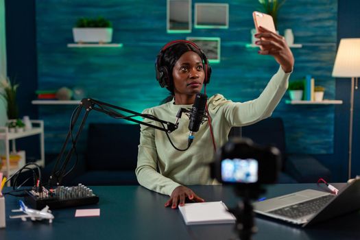 African content creator taking photo with smartphone for fans and recording broadcast. On-air online production internet podcast show host streaming live content, recording digital social media.