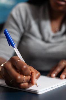 Closeup of student with dark skin writing university homework on notebook during communication online course. African american woman working remote from home at academic ideas using elearning platform