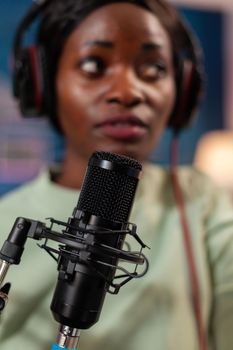 African host of online show using microphone talking with listeners entertainment. Speaking during livestreaming, blogger discussing in podcast wearing headphones.