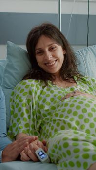 Caucasian couple waiting for child delivery in maternity ward at hospital. Young pregnant woman laying in bed and happy husband holding hand waiting for baby and parenthood lifestyle