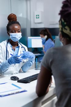 African american therapist doctor discussing with sick patient during clinical consultation explaining medical signing paperwork in hospital office. Women wearing protective face mask against covid19