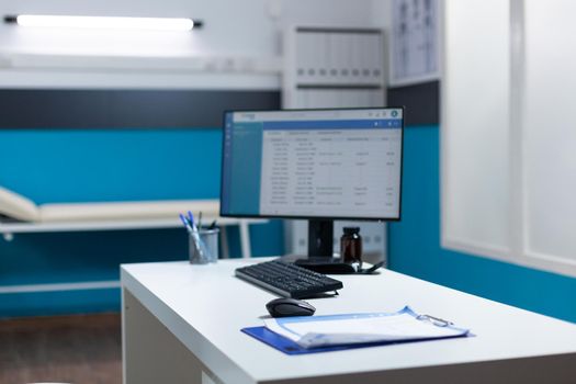 Empty desk with table medical paperwork and clinical appointment on computer screen in hospital office. Illuminated cabient with modern furniture. Space with nobody in it. Healthcare service