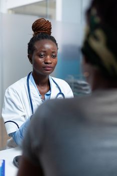 African american therapist doctor discussing sickness symptoms with sick patient prescribing medication treatment during clinical appointment. Practitioner woman working in hospital office