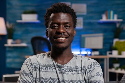 Portrait of african american employee looking into camera while resting on sofa enjoying spending free time alone at home. Young entrepreneur working remote from home at business project