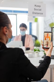 Business woman with face mask during video conference on smartphone, keeping social distancing as prevention against coronavirus flu during global pandemic. Using internet web video call chat message