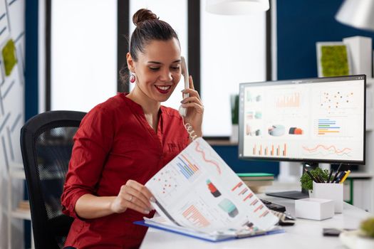 Businesswoman in company office checking finaicial statistics on clipboard, discusing details with coworkers during phone call conversation. Happy entrepreneur communicating with client.