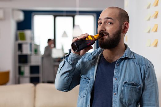 Man drinking bottle of beer after work meeting with colleagues for fun enjoyment. Cheerful celebration with coworkers at office while eating and drinking alcohol. Happy friends partying