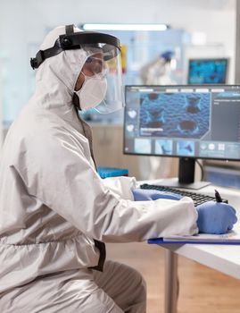 Biochemistry scientist dressed in ppe suit during epidemic experiment. Examining vaccine evolution using high tech technology and chemistry tools for scientific research virus development.