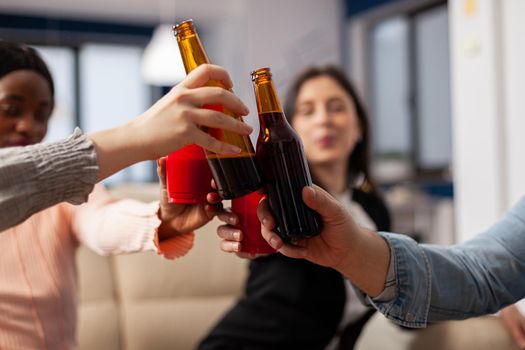 Close up of bottles and cups of beer from cheerful friends after work at office party. Multi ethnic happy group cheers for celebrating entertainment indoors with snacks drinks food