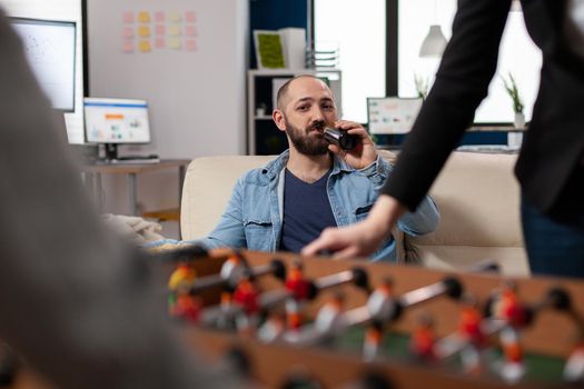 Man having fun while drinking beer after work at office watching foosball soccer football game. Worker enjoying alcohol drinks with firends colleagues, entertainment activity together