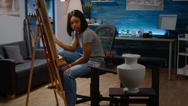 Artist of african american ethnicity reproducing vase design on white canvas for fine art masterpiece in studio at home. Black woman working on creative drawing as successful hobby