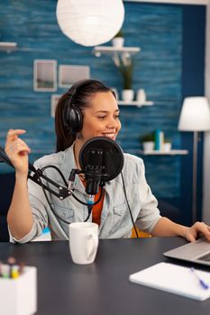 Vlogger looking at laptop while asking her audience to subscribe on her youtube channel. Digital influcencer recording talk show using modern equipment in home studio podcast