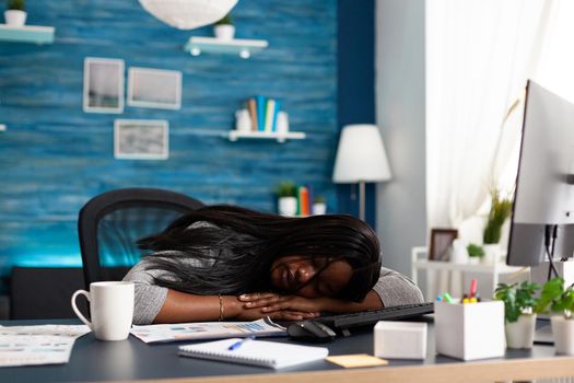 Exhausted tired workaholic black student sleeping on desk table in living room after working at deadline. Workaholic overworked disappointed african woman searching online business course