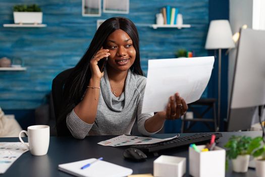Black student discussing with collegue at phone analyzing university paperwork with academic course sitting at desk working remote from home. African woman using university elearning platform