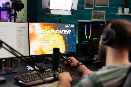 Back view of upseted streamer playing game competition using professional setup with streaming chat open. Gamer sitting on gaming chair using wireless controller and professional headphone