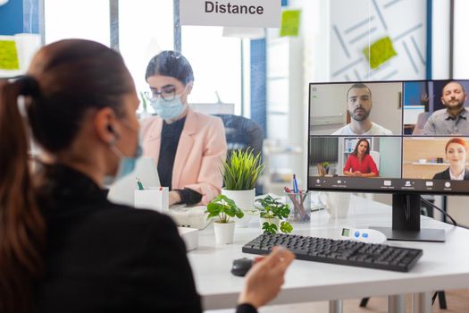 Businesswoman during remove video conference on computer wearing face mask as safety precaution during global pandemic with covid19 flu in new normal workplace. Online web internet virtual videocall