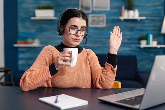 Student holding cup of coffee while listening her teacher during video call conference on laptop computer. Woman studying communication information using e-learning college platform