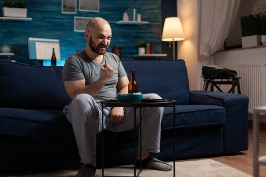 Football fan watching sport game championship supporting team raising hands after winning sports competition, eating popcorn. Excited soccer man celebrating good championship in living room