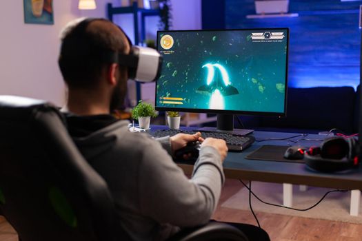 Professional gamer wearing virtual realilty headset and playing space shooter video games with controller. Man streaming online videogames for esport tournament in room with neon lights