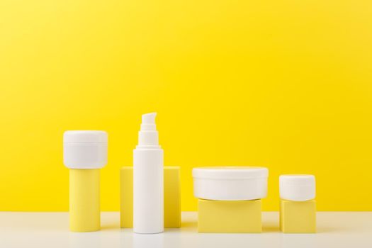 Trendy colorful composition with set of cosmetic bottles with beauty products on geometric props against yellow background with copy space. Concept of creams with citrus extracts or skin products with sunblock