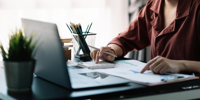 Business woman using calculator and laptop for do math finance on wooden desk in office and business working background, tax, accounting, statistics and analytic research concept.