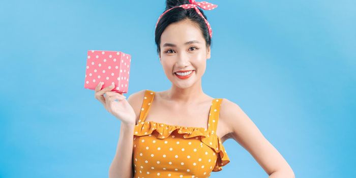 Happy pretty woman in dress holding little box isolated on a blue background